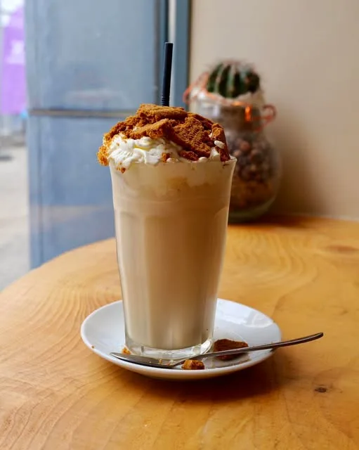 Latte glacé surmonté de chantilly et de spéculoos émietté, posé sur une table en bois